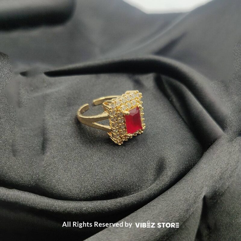 Adjustable Red Gemstone Ring with Gold-Toned Finish 2 Adjustable ring with a red gemstone and gold-toned finish on a black fabric background