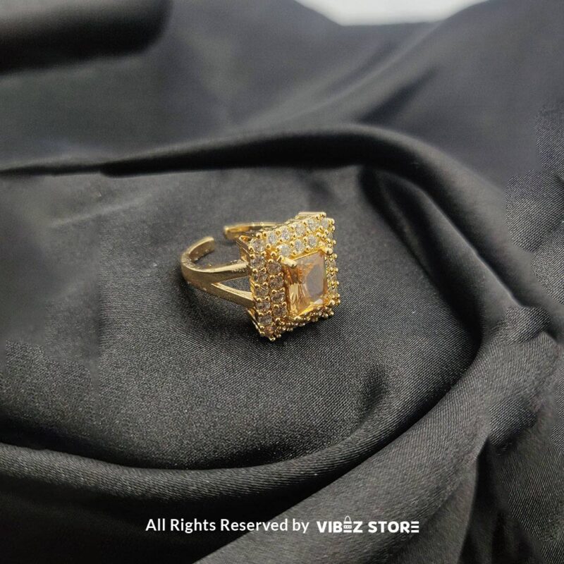 Adjustable Red Gemstone Ring with Gold-Toned Finish 1 Adjustable ring with a red gemstone and gold-toned finish on a black fabric background