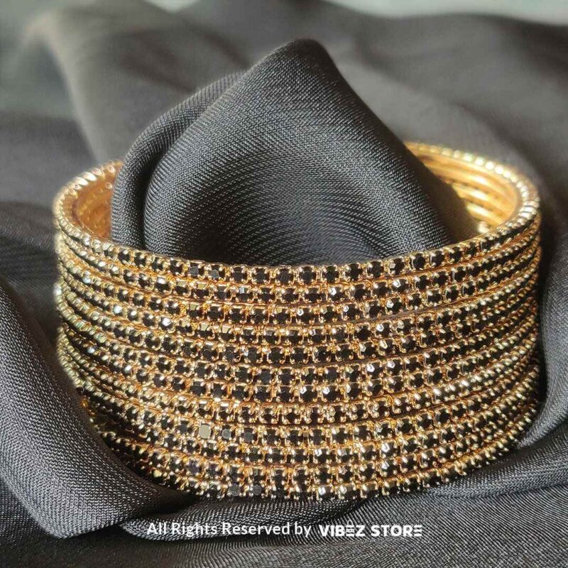 Multi-Layer Black Crystal Gold Bangle Set 1 Multi-layer gold bangle set with black crystal accents on a black fabric background