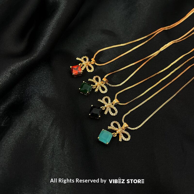 Bow-Embellished Square Gemstone Locket 1 Bow-adorned Square Gemstone Locket in red, green, black, and turquoise colors with gold chains on a black background