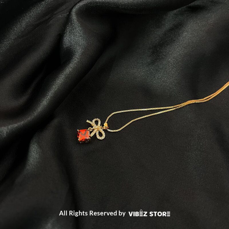 Bow-Embellished Square Gemstone Locket 5 Bow-adorned Square Gemstone Locket in red, green, black, and turquoise colors with gold chains on a black background