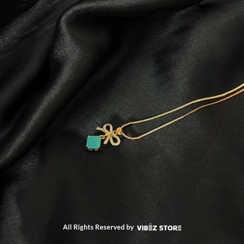 Bow-Embellished Square Gemstone Locket 2 Bow-adorned Square Gemstone Locket in red, green, black, and turquoise colors with gold chains on a black background