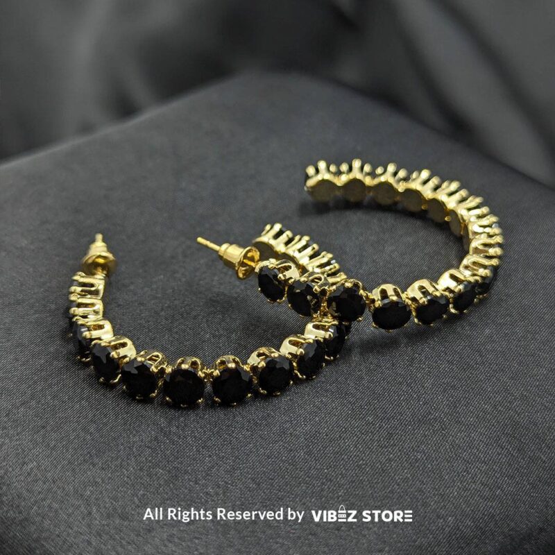 Black Crystal Gold-Tone Hoop Earrings 1 Black crystal gold-tone hoop earrings with a shimmering design displayed elegantly on a black satin fabric.