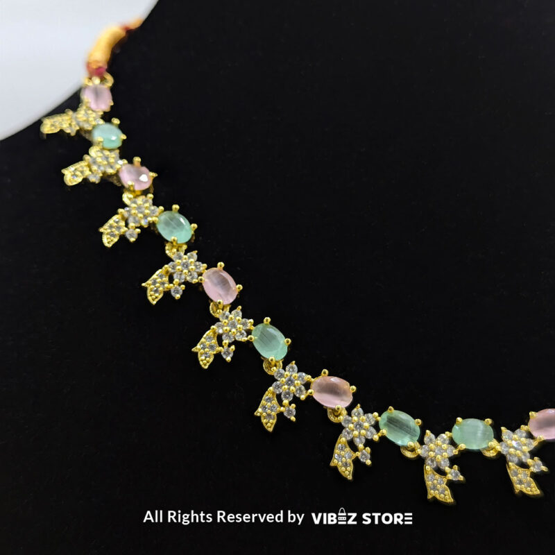Gold-Plated Pastel Gemstone Necklace Set with Earrings 4 Gold-plated pastel gemstone necklace with matching drop earrings on a black display, featuring pink and green stones in floral motifs, ideal for weddings and festive occasions.