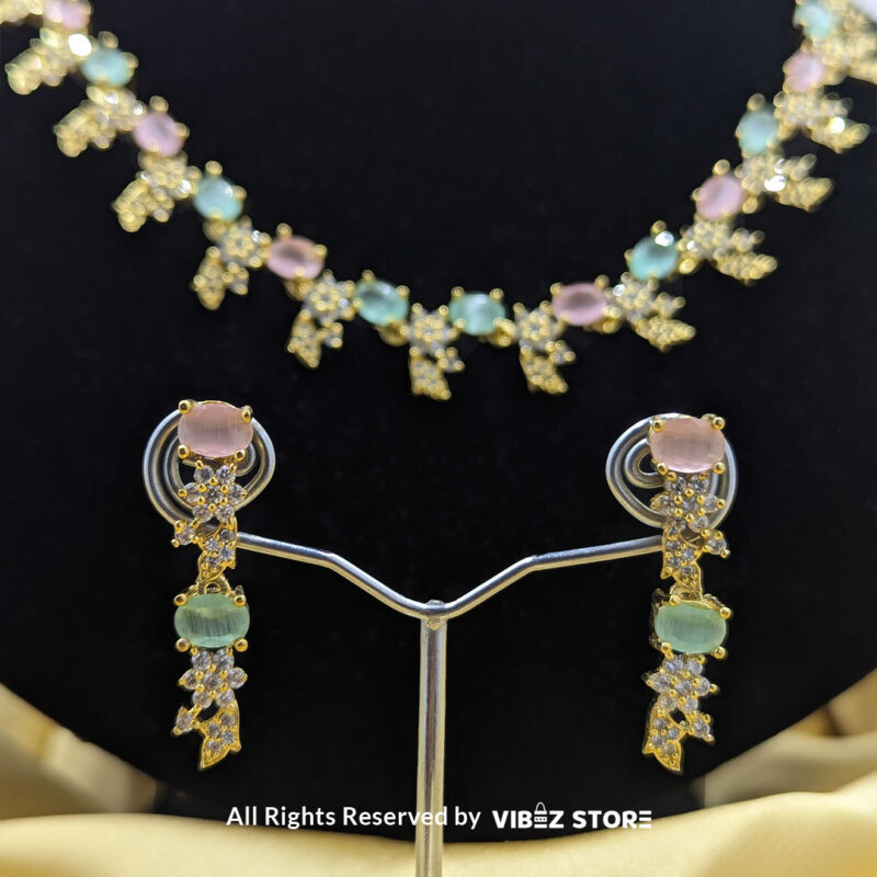 Gold-Plated Pastel Gemstone Necklace Set with Earrings 5 Gold-plated pastel gemstone necklace with matching drop earrings on a black display, featuring pink and green stones in floral motifs, ideal for weddings and festive occasions.
