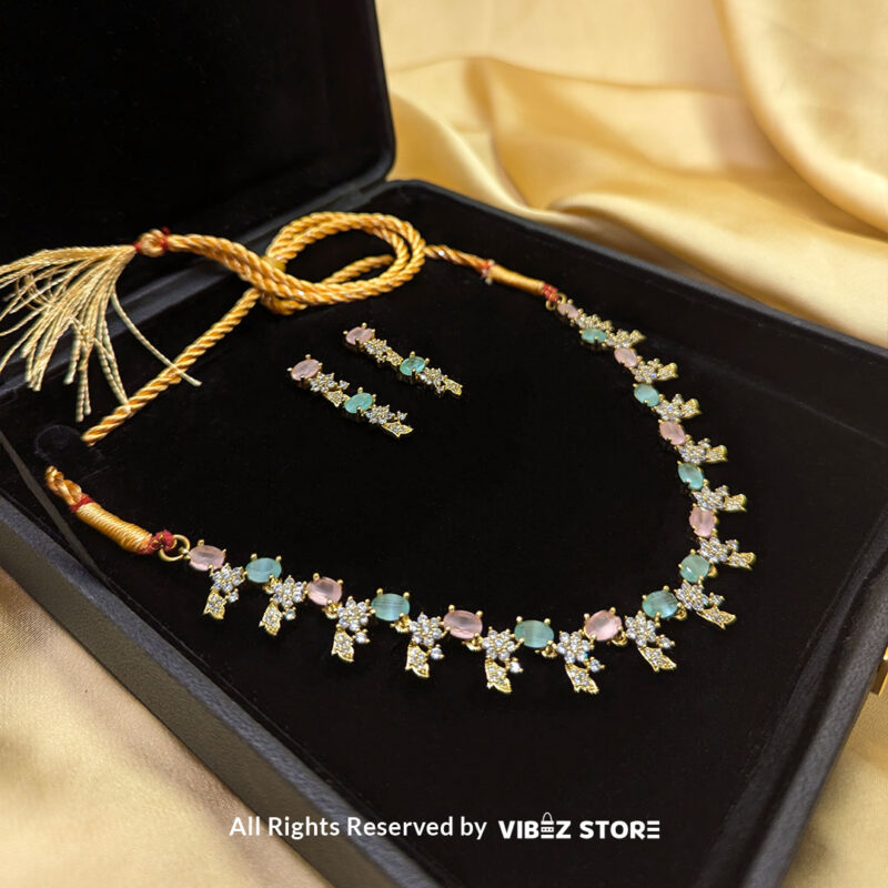 Gold-Plated Pastel Gemstone Necklace Set with Earrings 2 Gold-plated pastel gemstone necklace with matching drop earrings on a black display, featuring pink and green stones in floral motifs, ideal for weddings and festive occasions.