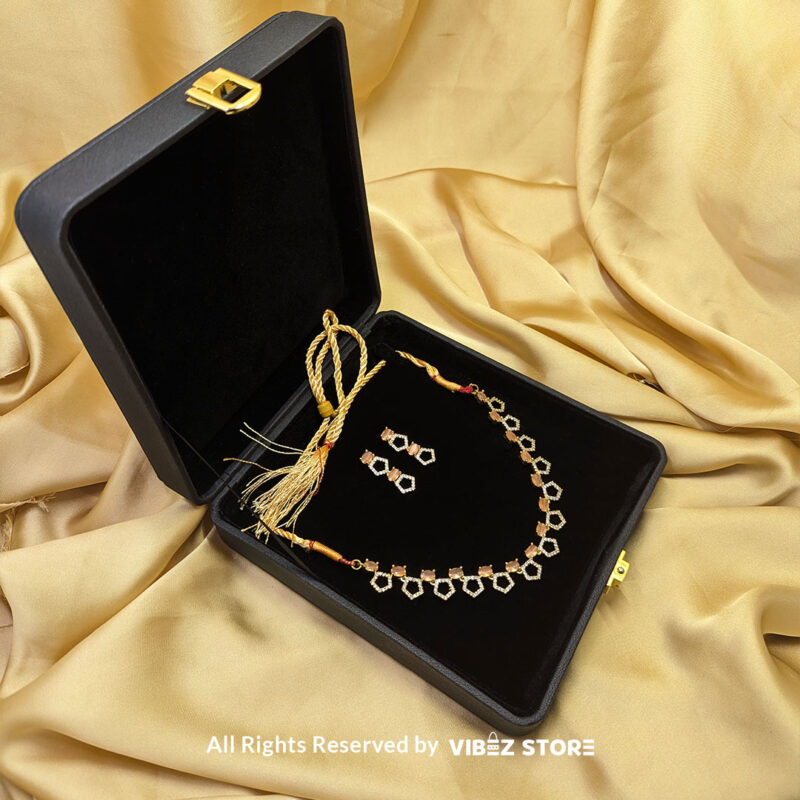 Gold-Plated Peach Gemstone Necklace Set with Earrings 1 Gold-plated necklace set featuring peach gemstones and a hexagonal design, paired with matching drop earrings on a black display, perfect for weddings and parties.