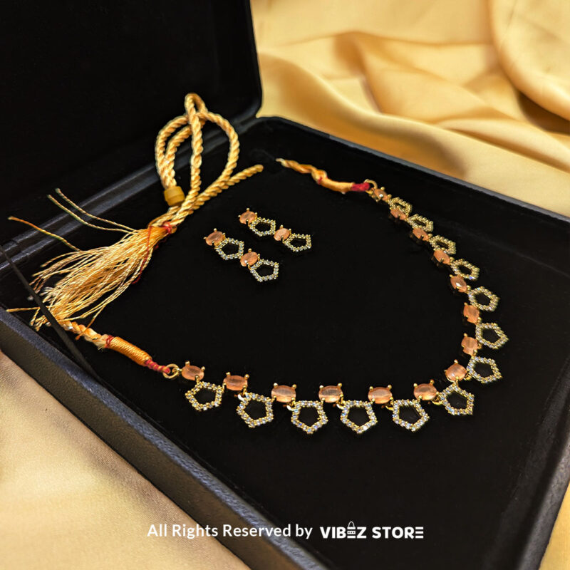 Gold-Plated Peach Gemstone Necklace Set with Earrings 2 Gold-plated necklace set featuring peach gemstones and a hexagonal design, paired with matching drop earrings on a black display, perfect for weddings and parties.