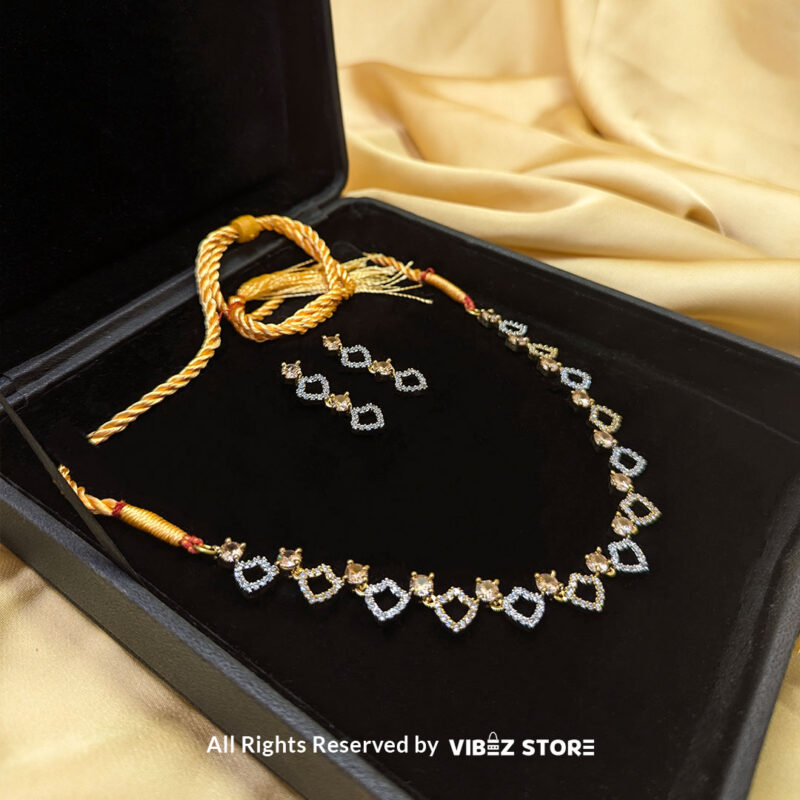 Heart Design Necklace Set with Earrings 2 Heart-shaped necklace set with sparkling stones and matching earrings, displayed on a black mannequin with a golden fabric backdrop.