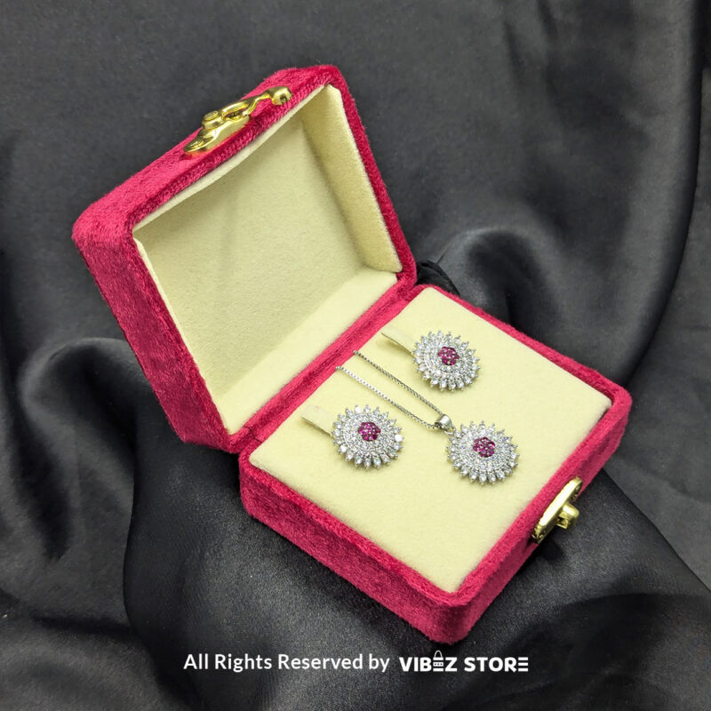Ruby Starburst Pendant and Earrings Set 3 Ruby starburst pendant with matching earrings, featuring shimmering crystals and a vibrant ruby centerpiece, displayed on a sleek black fabric.