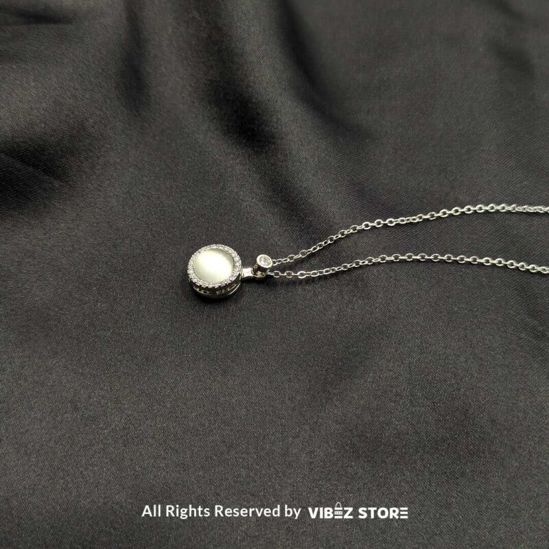 Elegant Rotating Pearl Locket Pendant with Sparkling Accents 2 A silver rotating pearl locket pendant surrounded by sparkling accents, displayed on a black fabric background.