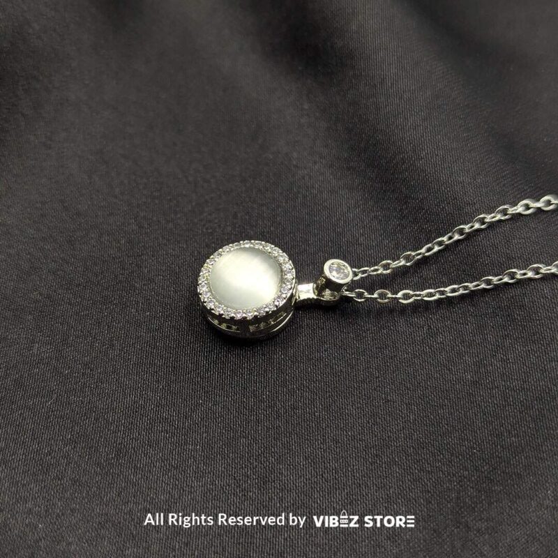 Elegant Rotating Pearl Locket Pendant with Sparkling Accents 1 A silver rotating pearl locket pendant surrounded by sparkling accents, displayed on a black fabric background.