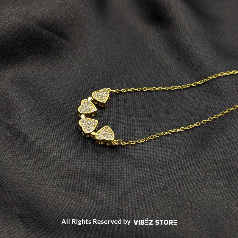 Magnetic Gold Heart Locket with Pave Crystal Design 2 Magnetic gold-tone locket with interconnected heart shapes adorned with pave crystals, displayed on a black fabric background.