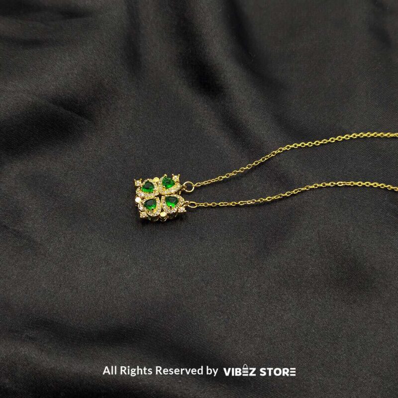 Magnetic Heart-Shaped Gold Locket with Green Gemstones 3 Gold magnetic heart-shaped locket featuring green gemstones and pave crystals, displayed on a black fabric background.