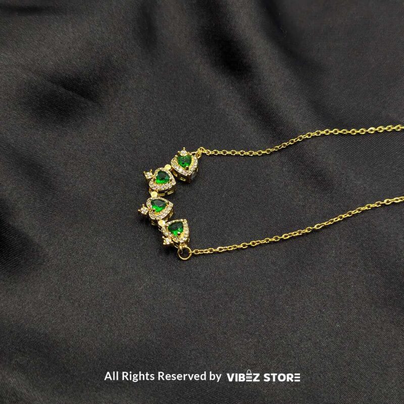 Magnetic Heart-Shaped Gold Locket with Green Gemstones 2 Gold magnetic heart-shaped locket featuring green gemstones and pave crystals, displayed on a black fabric background.