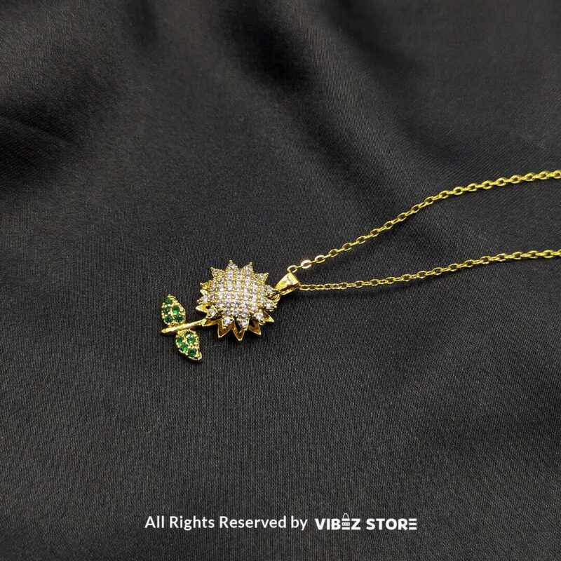 Elegant Rotating Sunflower Locket Pendant with Green Leaf Design 1 A gold rotating sunflower locket pendant with sparkling stones and green leaf accents displayed on a black fabric background.