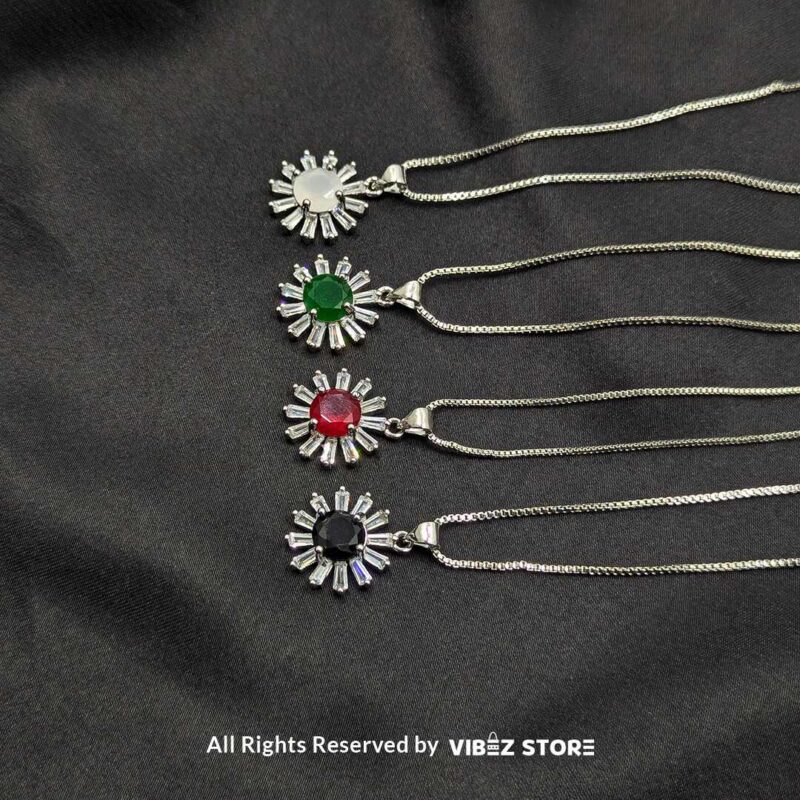 Radiant Sunburst Gemstone Locket Collection 1 A collection of silver sunburst lockets featuring vibrant gemstones in white, green, red, and black, laid on a black fabric background.