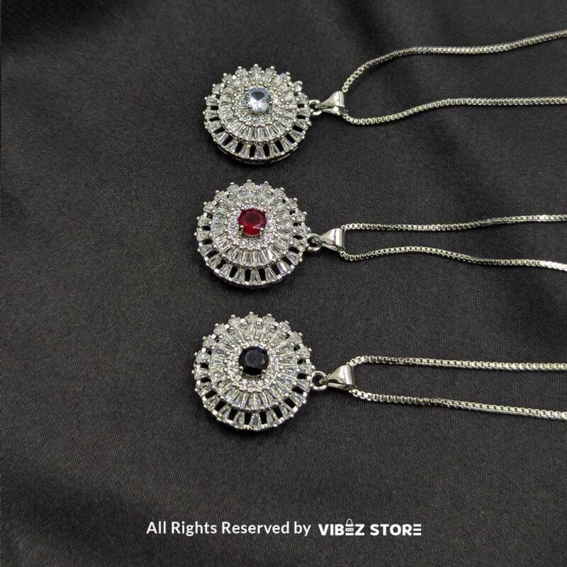 Gemstone Round Locket with Crystal Halo 1 A silver-tone round locket with a vibrant gemstone (choose ruby red, sapphire blue, or clear crystal) surrounded by intricate crystal detailing, displayed on a black fabric background.
