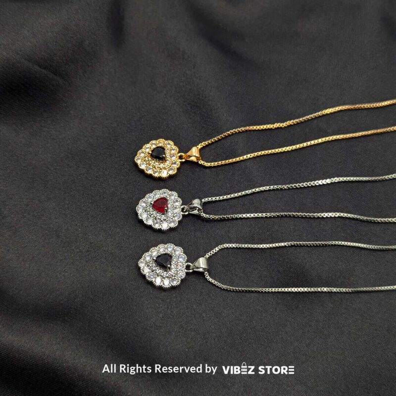 Heart-Shaped Gemstone Locket with Crystal Accents 1 Three heart-shaped gemstone lockets in black and red, framed by dazzling crystals, displayed with gold-tone and silver-tone chains on a black fabric background.