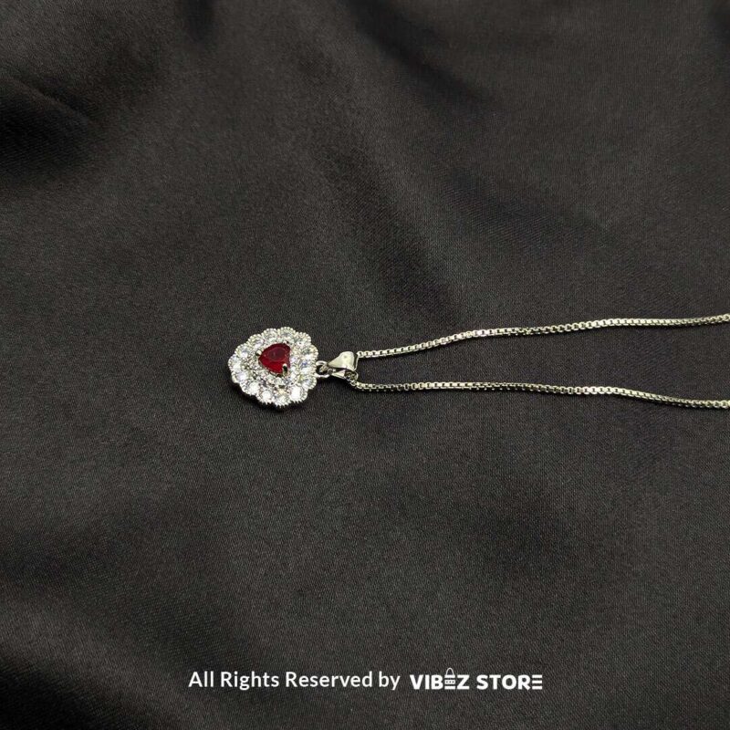 Heart-Shaped Gemstone Locket with Crystal Accents 4 Three heart-shaped gemstone lockets in black and red, framed by dazzling crystals, displayed with gold-tone and silver-tone chains on a black fabric background.