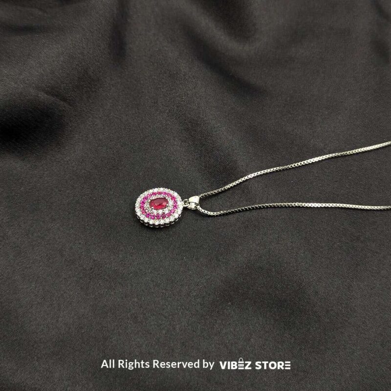 Pink Gemstone Halo Locket 2 A silver-tone locket featuring a pink gemstone surrounded by a double halo of crystals, displayed on a black fabric background.