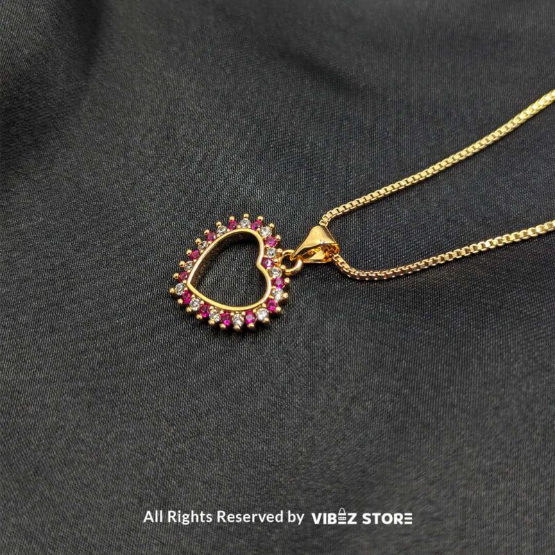 Gold Heart Frame Locket with Pink Gem Accents 1 Gold heart-shaped open-frame locket with pink gemstone accents displayed on a black fabric background.