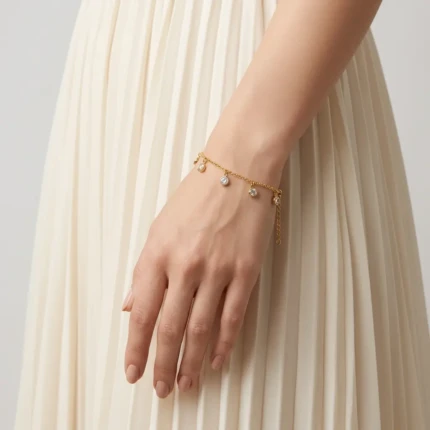 Model wearing gold crystal charm bracelet on wrist with cream outfit