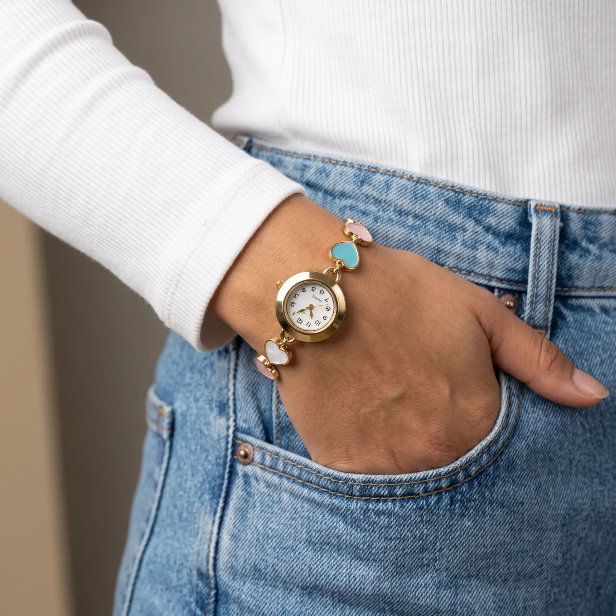 Gold-Tone Heart Charm Bracelet Watch for Women Woman wearing a gold-tone bracelet watch with pink blue and white heart charms