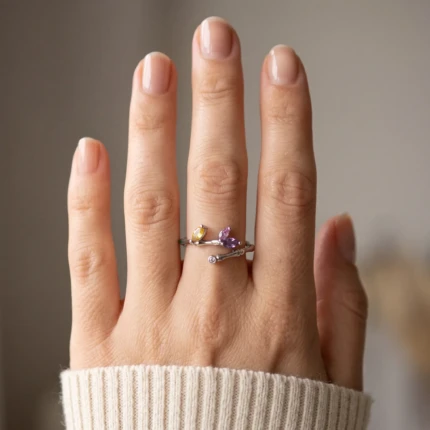 Woman wearing a silver-tone leaf ring with purple and yellow crystals